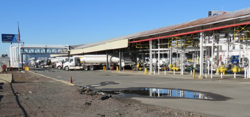 This figure shows two images of tank trucks being loaded with fuel for delivery. The first show a semi-trailer being loaded with gasoline and the second shows a single-unit truck being loaded with home heating oil. 1 of 2.